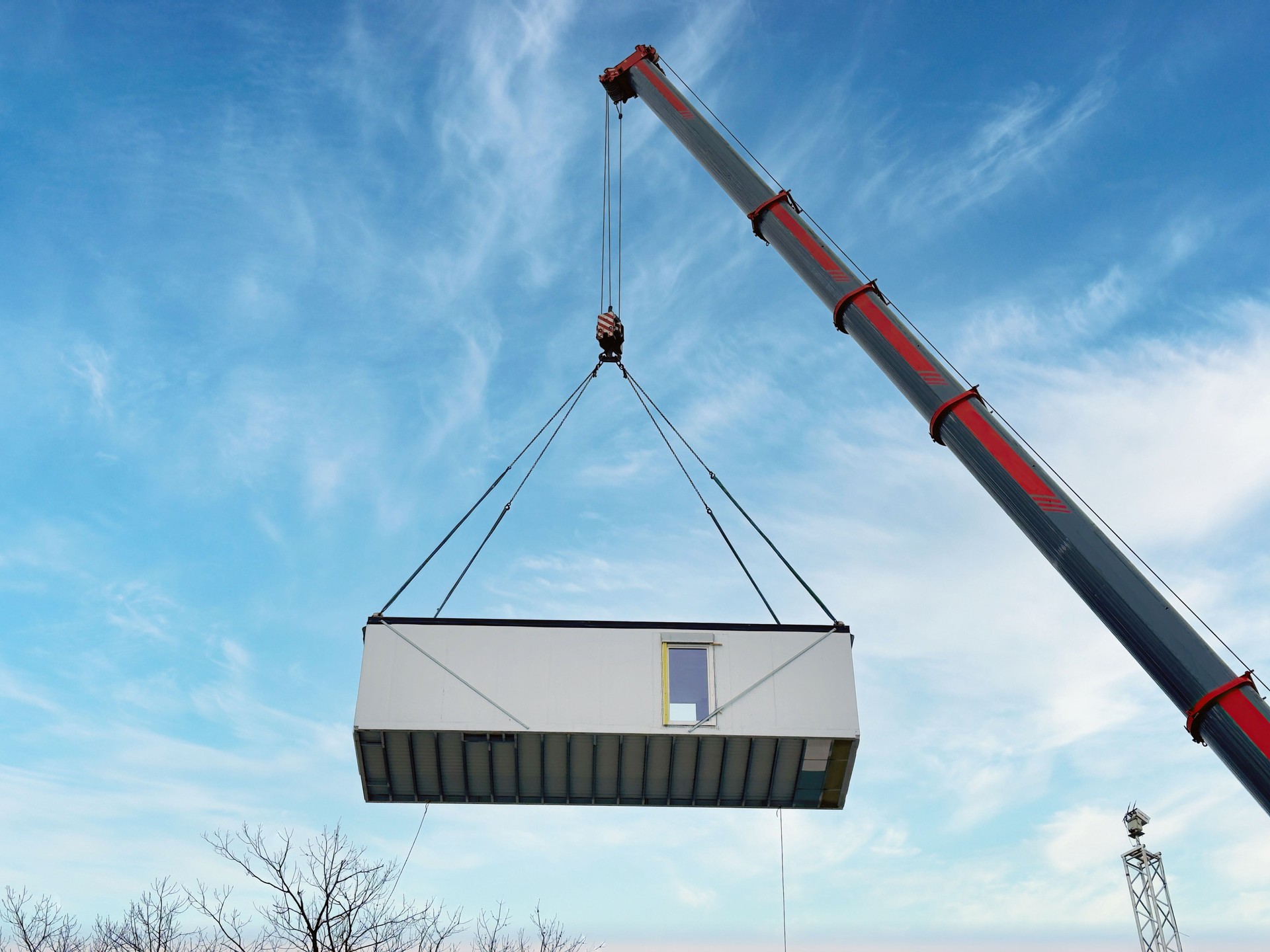 large crane lifting a prefabricated modular building unit against a bright blue sky